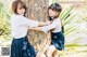 Two young girls leaning against a tree in a park.