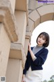 A woman leaning against a stone wall wearing a blue cardigan.