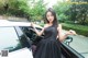 A woman in a black dress standing next to a white car.