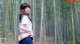 A woman in a school uniform standing in a bamboo forest.