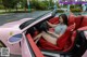 A woman sitting in the driver's seat of a pink sports car.