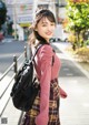 A woman in a pink sweater and plaid skirt with a backpack.