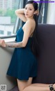 A woman in a blue dress leaning against a window.
